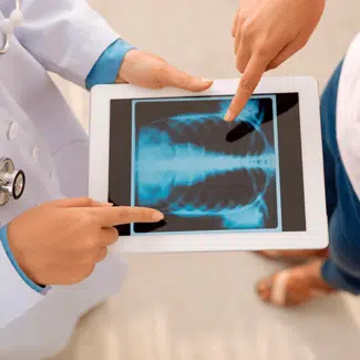 Médico sosteniendo un ipad blanco con rayos X en la pantalla explicando a una paciente