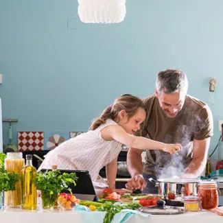 hija sentada en la encimera ayudando a su padre a cocinar la cena con la comida a su alrededor