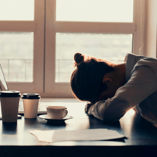 Mujer con cansancio y varias tazas de café apoyando la cabeza en el escritorio
