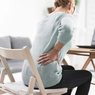 mujer sentada en una silla inclinada hacia delante mientras se sujeta la cadera