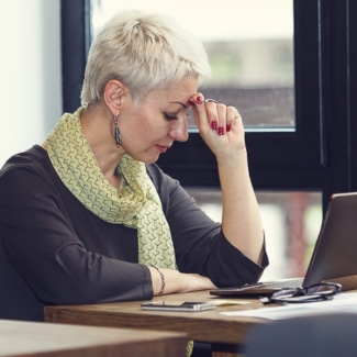 Mujer con dolor de cabeza tratando de trabajar en el ordenador portátil