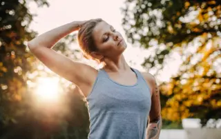 Portrait of healthy young woman stretching her neck outdoors. Caucasian fitness model warming up in park.