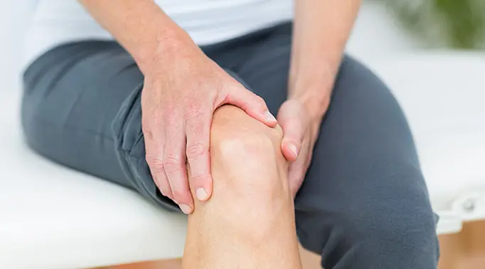 Person holding their knee in pain while sitting on a massage table