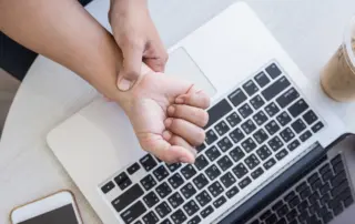 Person rubbing wrist in pain while working on computer