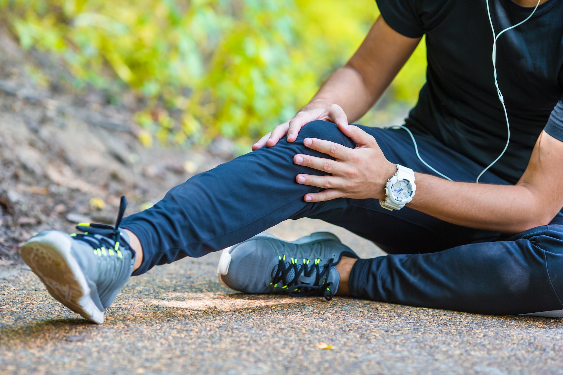 male runner sits on ground holding knee in pain