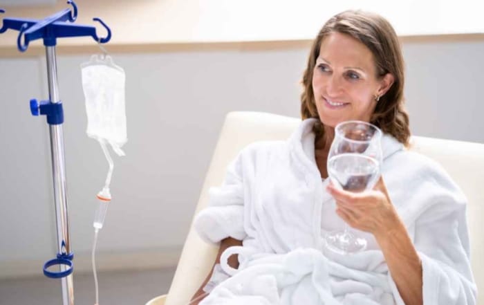 lady in medical clinic with IV drip drinking a glass of water, smiling