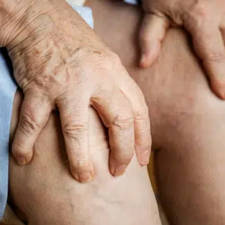 Man holding knee in pain with arthritic hands