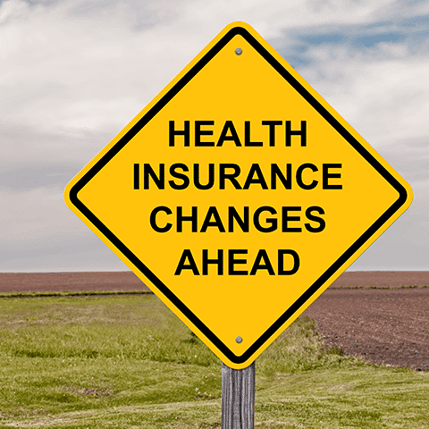 Yellow road sign in a field stating health insurance changes ahead