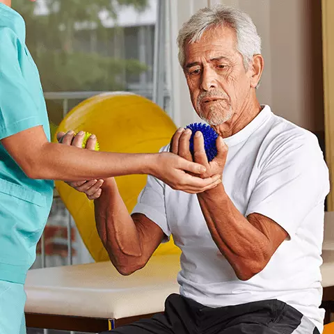 Hombre mayor con pelotas de punta en las manos trabajando con un fisioterapeuta