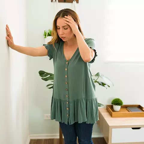 Woman is using her hand to support herself against a wall while holder her head