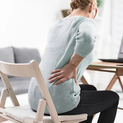 woman sitting in a chair leaning forward while holding her hip