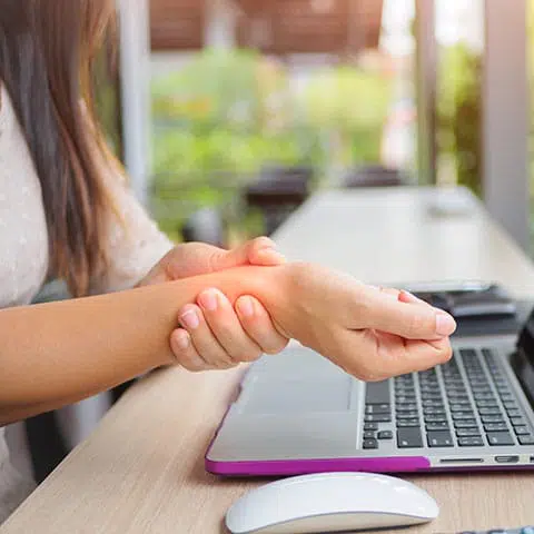 Woman holding wirst over laptop with a purple case and a computer mouse sitting next to the laptop