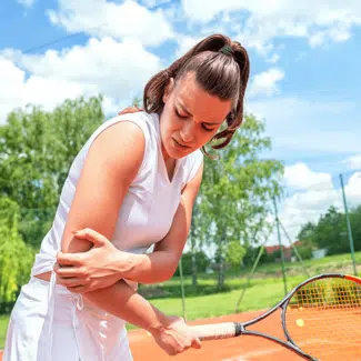 woman in white holding a tennis racket while gripping her elbow in pain